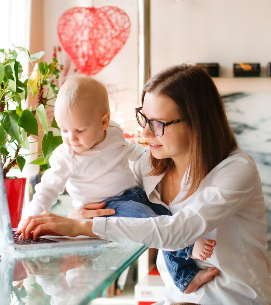 Caucasian emotional mom woman with glasses at laptop computer in the kitchen with baby